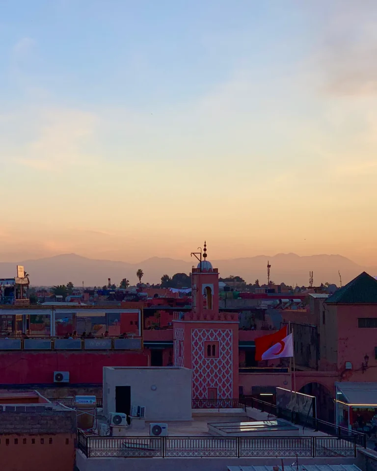 Blick über rosa Gebäude in Marrakesch zum Atlasgebirge bei Sonnenuntergang.