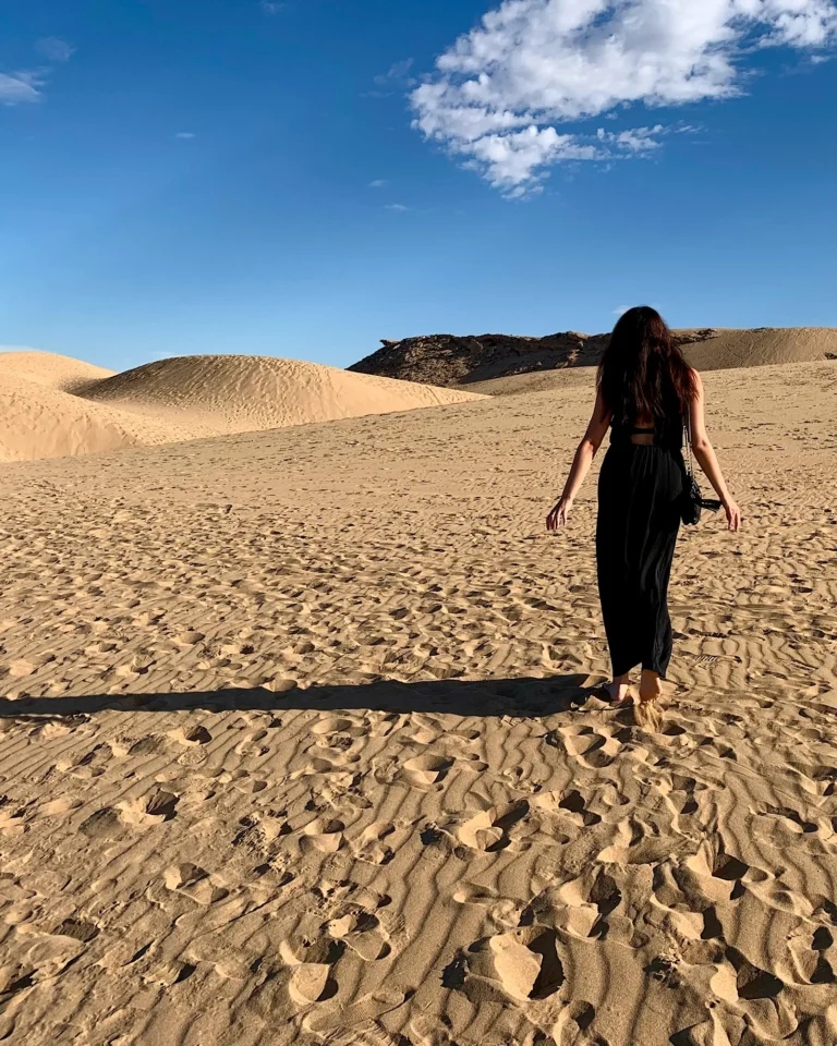 Frau im schwarzen Kleid läuft durch die Sanddünen von Tamri nahe Agadir (Rückenansicht).