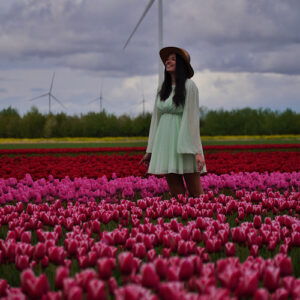 A woman standing sideways in a tulip field in Flevoland, enjoying the spring breeze among pink, white and red flowers.