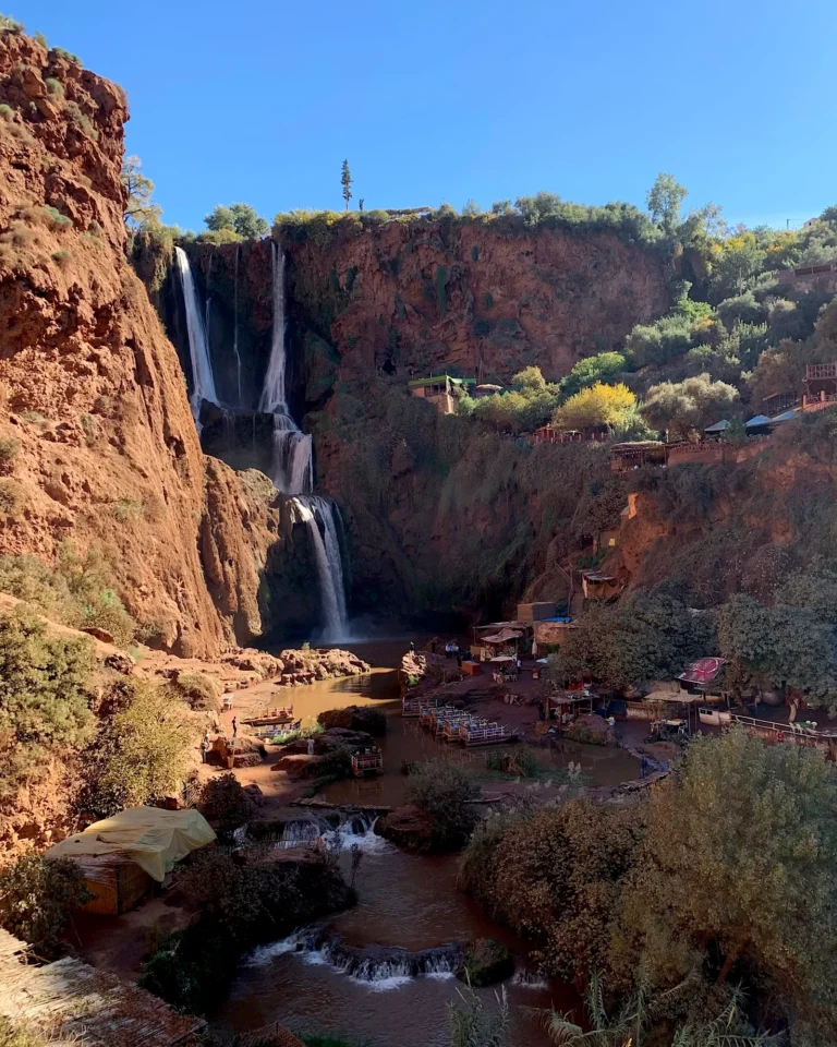 Blick vom Tal nach oben auf die Ouzoud-Wasserfälle mit Fluss und Booten.