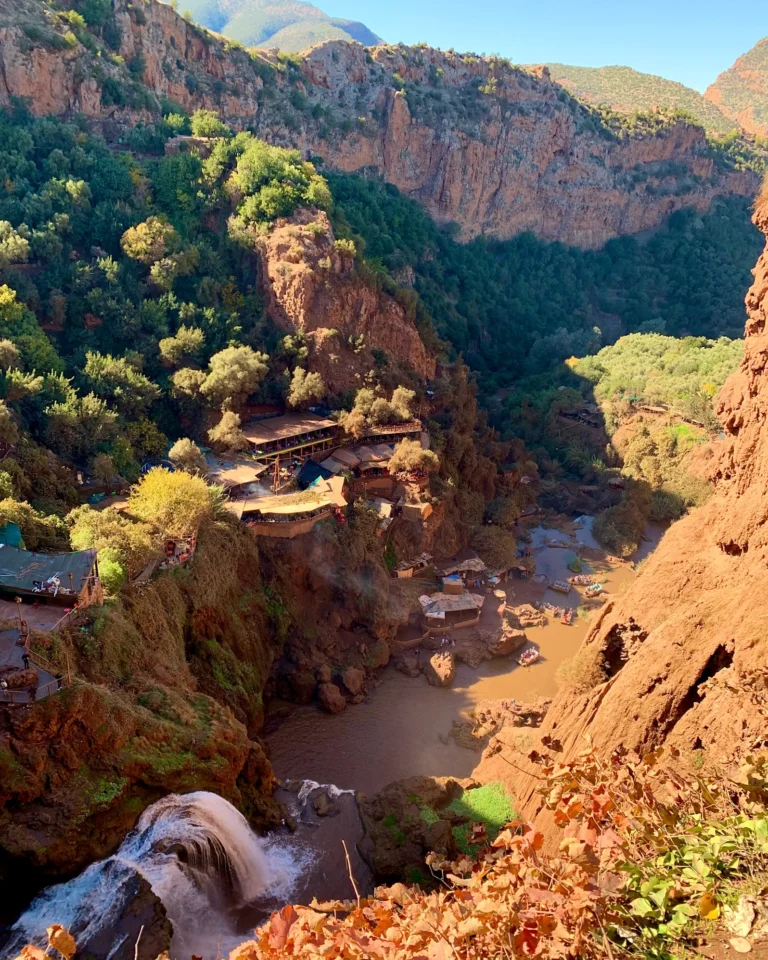 Blick von oben in das hellbraune Tal der Ouzoud-Wasserfälle mit kleinen Hütten.