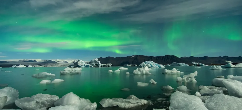 Eisblöcke treiben friedlich im Diamond Beach See, während die lebendigen Polarlichter darüber leuchten, Island.