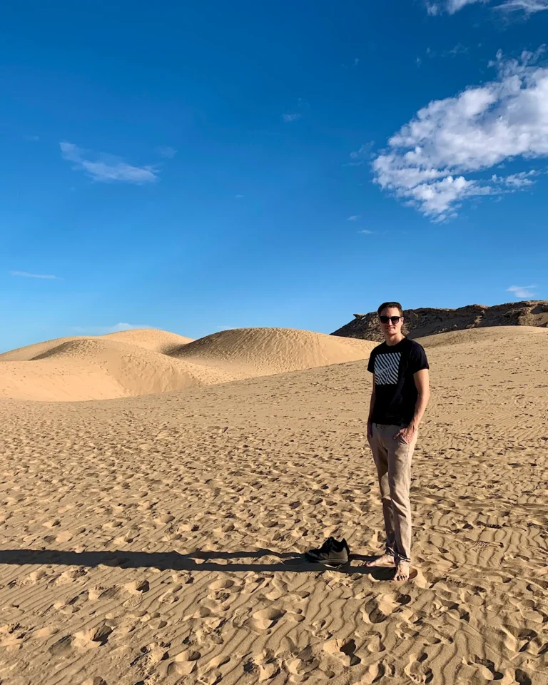 Junger Mann steht in den Sanddünen von Agadir und schaut in die Kamera.