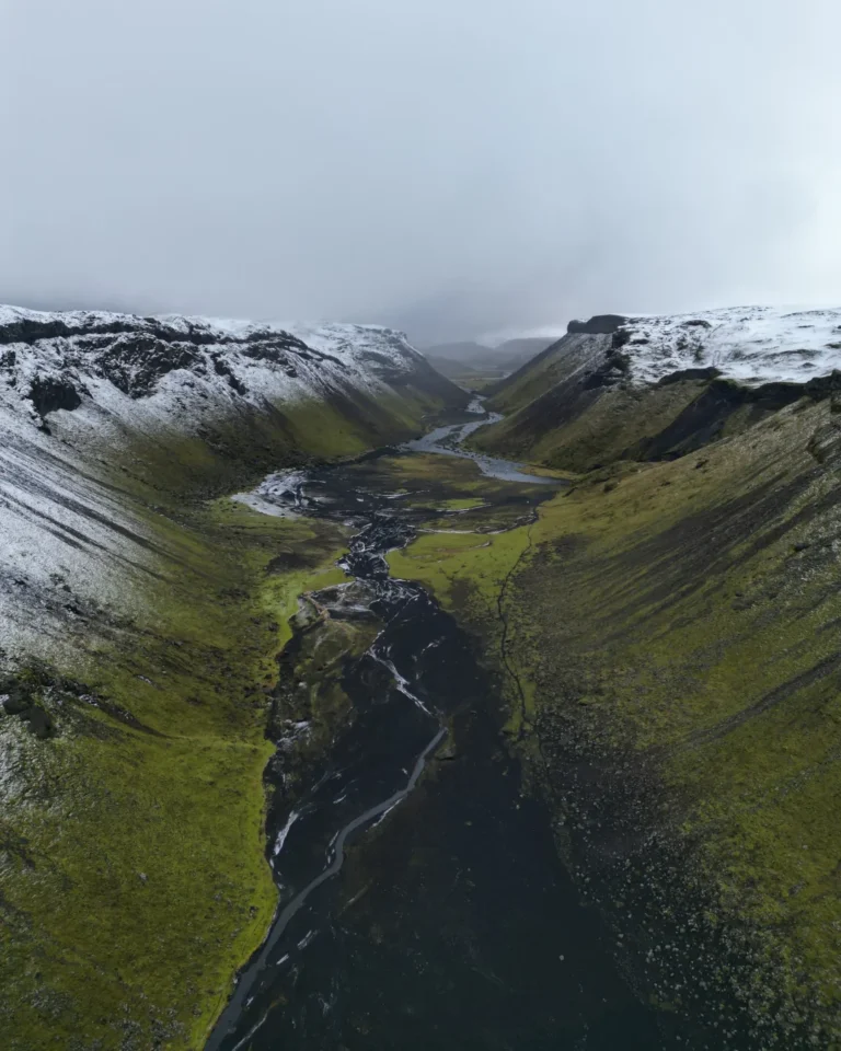 View of Eldgjá Canyon framed by snow-capped mountains and lush green grassland, Iceland