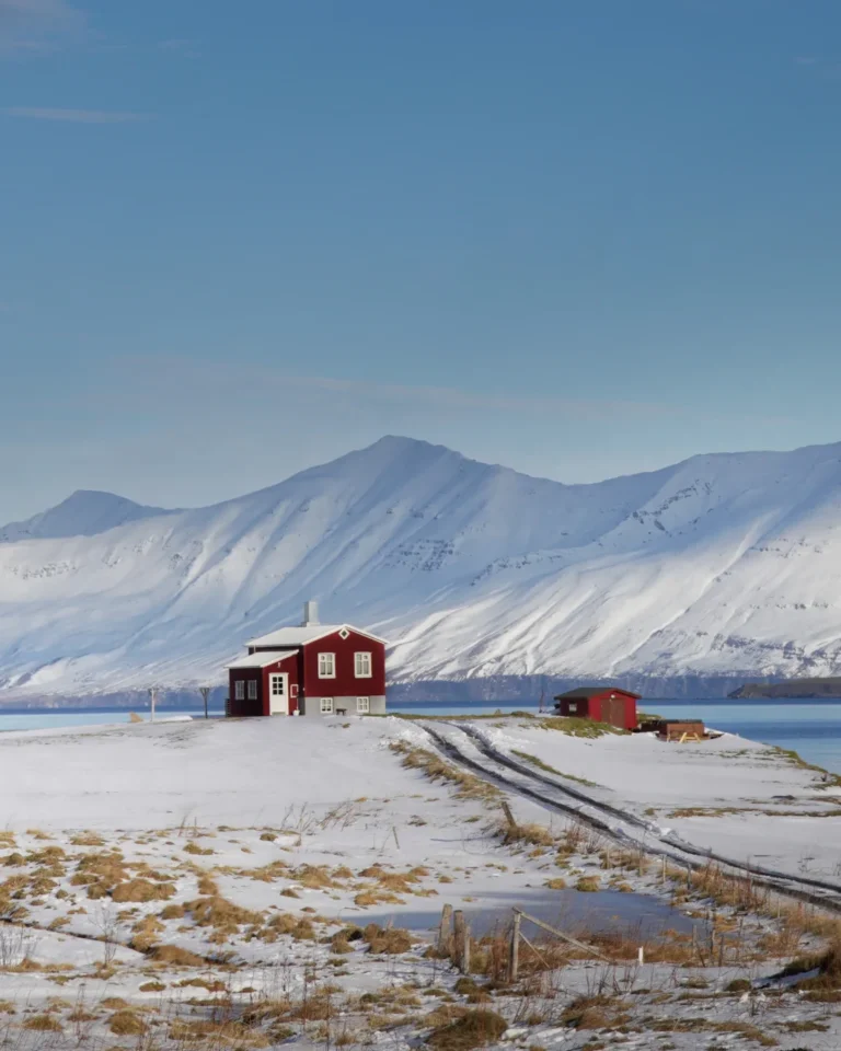 A red house surrounded by snowy mountains near Dalvík, Iceland, on a bright winter day