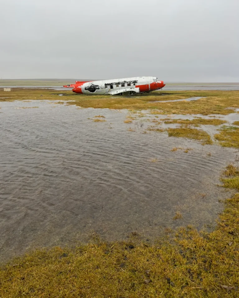 The red-colored wreck of a DC-3 plane at Eyvindarholt, set against the Icelandic landscape