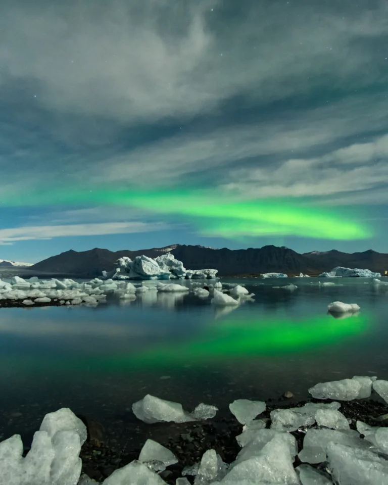 Ice blocks floating peacefully in Diamond Beach Lake, with the vibrant polar lights overhead, Iceland