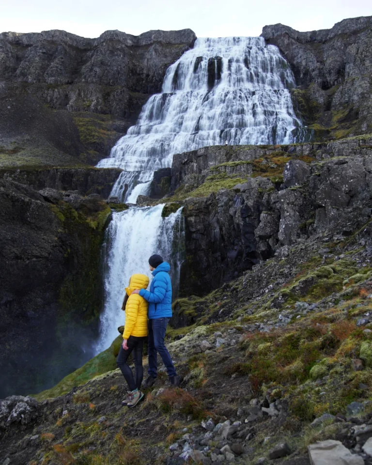 A couple standing together in front of the majestic Dynjandi Waterfall in Iceland