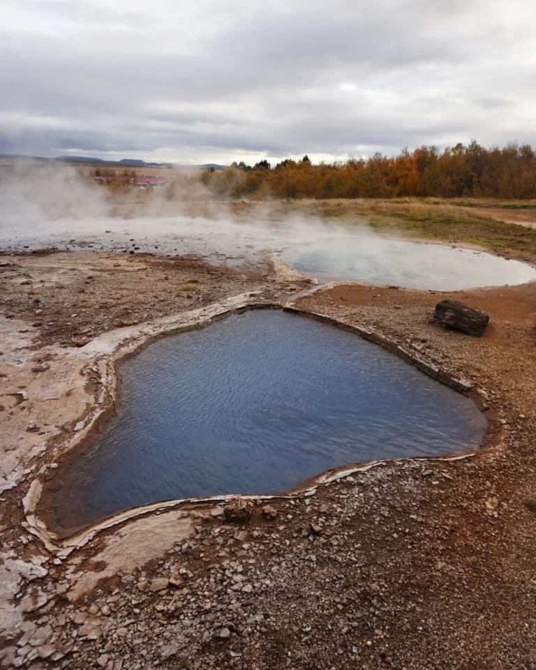 A steaming pond surrounded by geothermal activity in Haukadalur Geothermal Park, Iceland