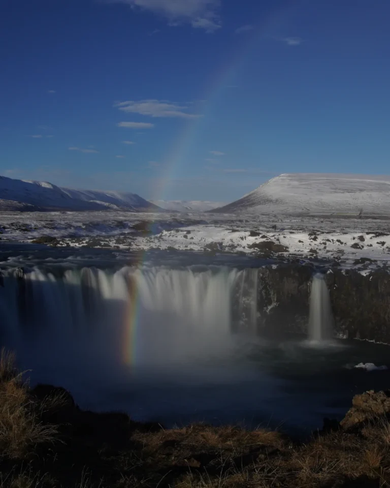 A stunning view of Goðafoss waterfall in Iceland, with a vibrant rainbow arching over the cascading water