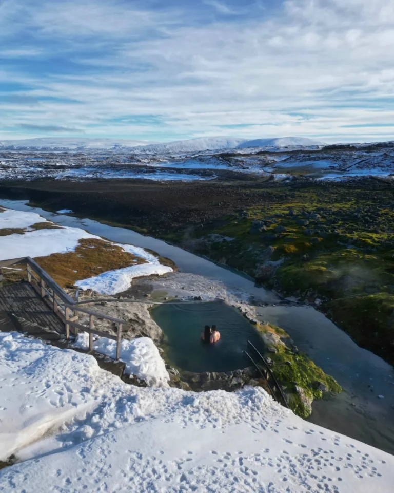 Two people bathing in a natural hot spring at Hveravellir in Iceland, surrounded by geothermal beauty