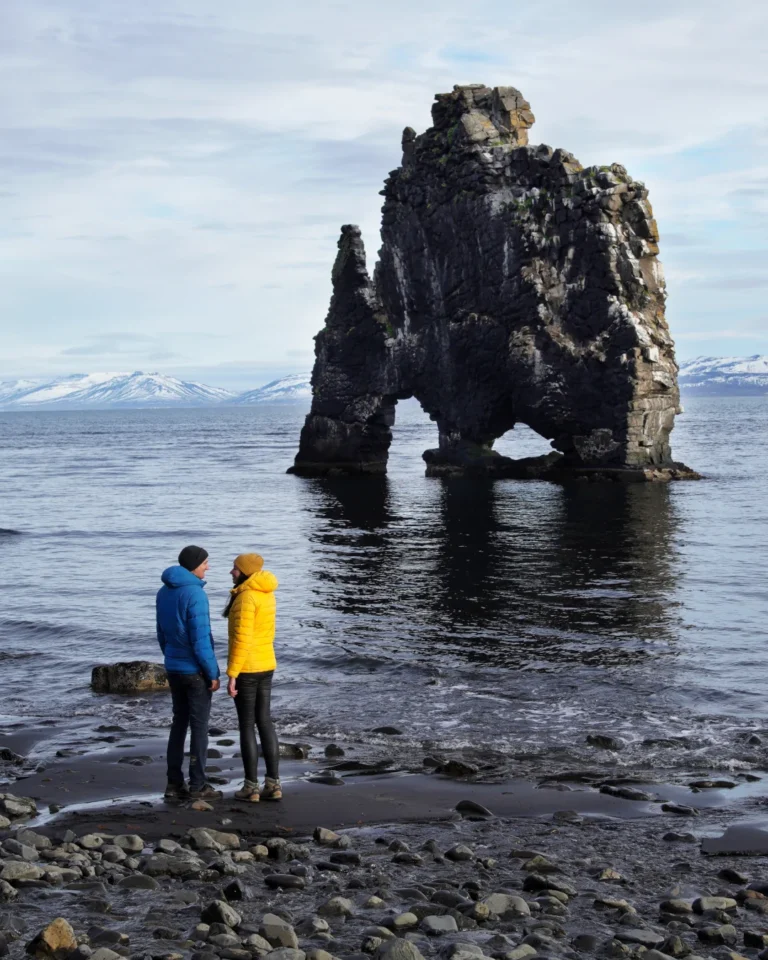 Two people standing in front of the Hvítserkur rock formation, Iceland