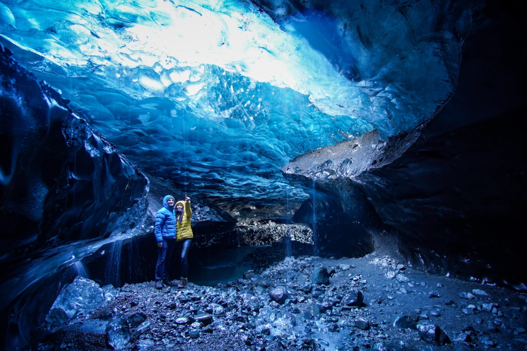 A couple inside Vatnajökull glacier, on there Iceland Adventure, surrounded by blue ice walls.