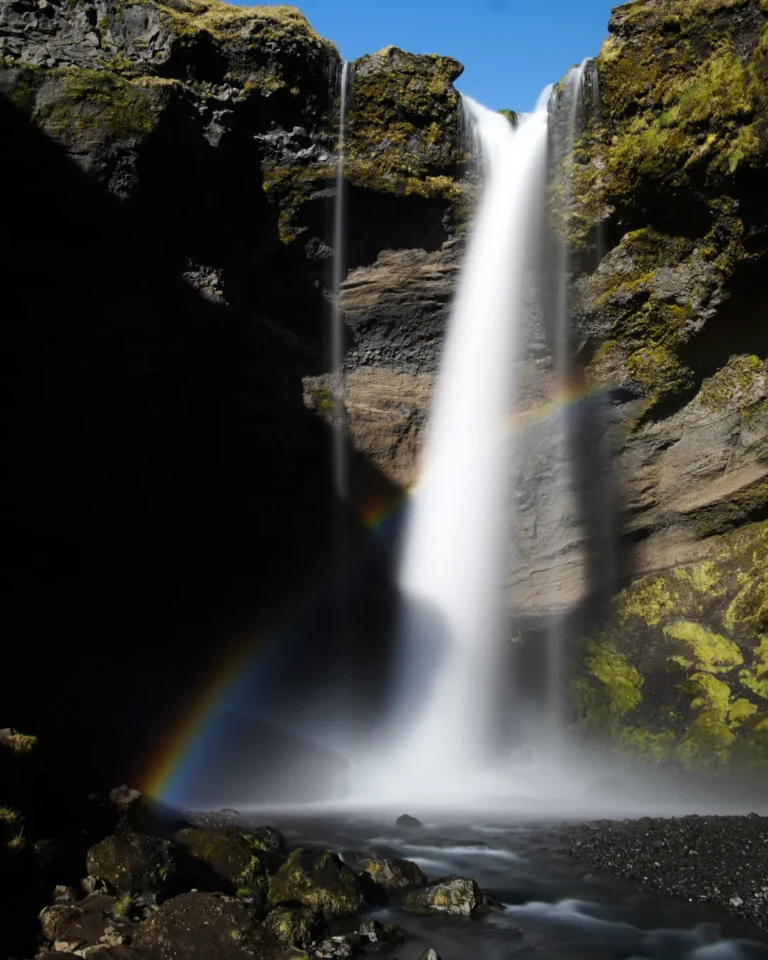 Kvernufoss waterfall cascading into a rocky pool with a small rainbow in the mist, Iceland