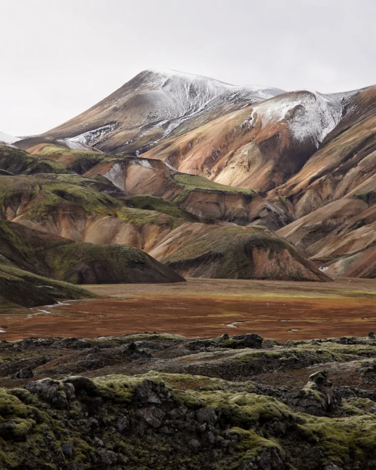 A telephoto view of the vibrant rhyolite mountains of Landmannalaugar, featuring a striking snowy peak