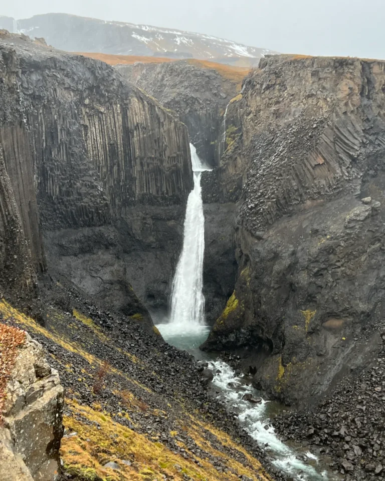 Litlanesfoss waterfall surrounded by grey rocks, with a light dusting of snow, Iceland