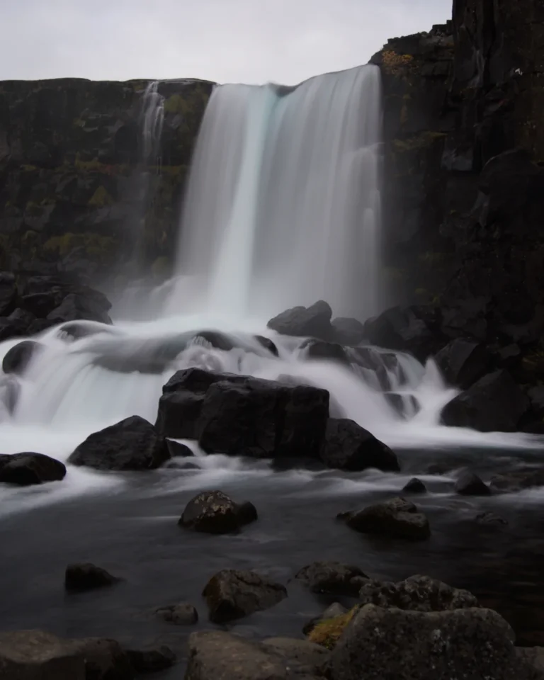 Oxararfoss waterfall surrounded by rocky cliffs and lush greenery in Thingvellir National Park, Iceland