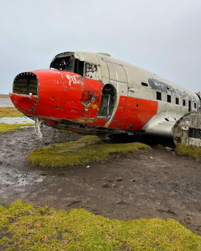 A striking red DC-3 plane wreck at Eyvindarholt, with the barren Icelandic landscape in the background