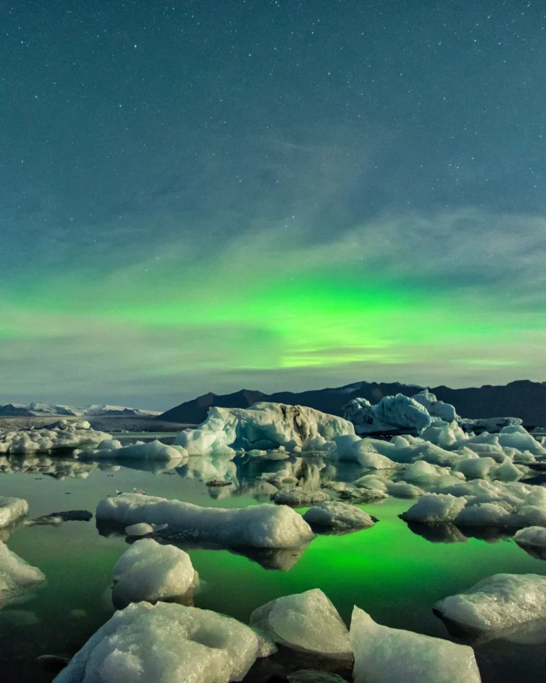 Stunning ice blocks floating in Diamond Beach Lake, illuminated by the vibrant polar lights above, Iceland