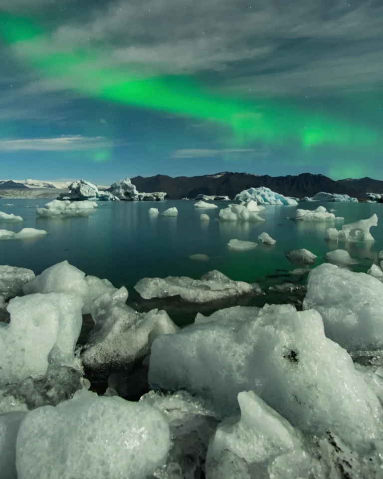 Beautiful polar lights shining above Diamond Beach Lake, casting a colorful glow on the floating ice blocks, Iceland