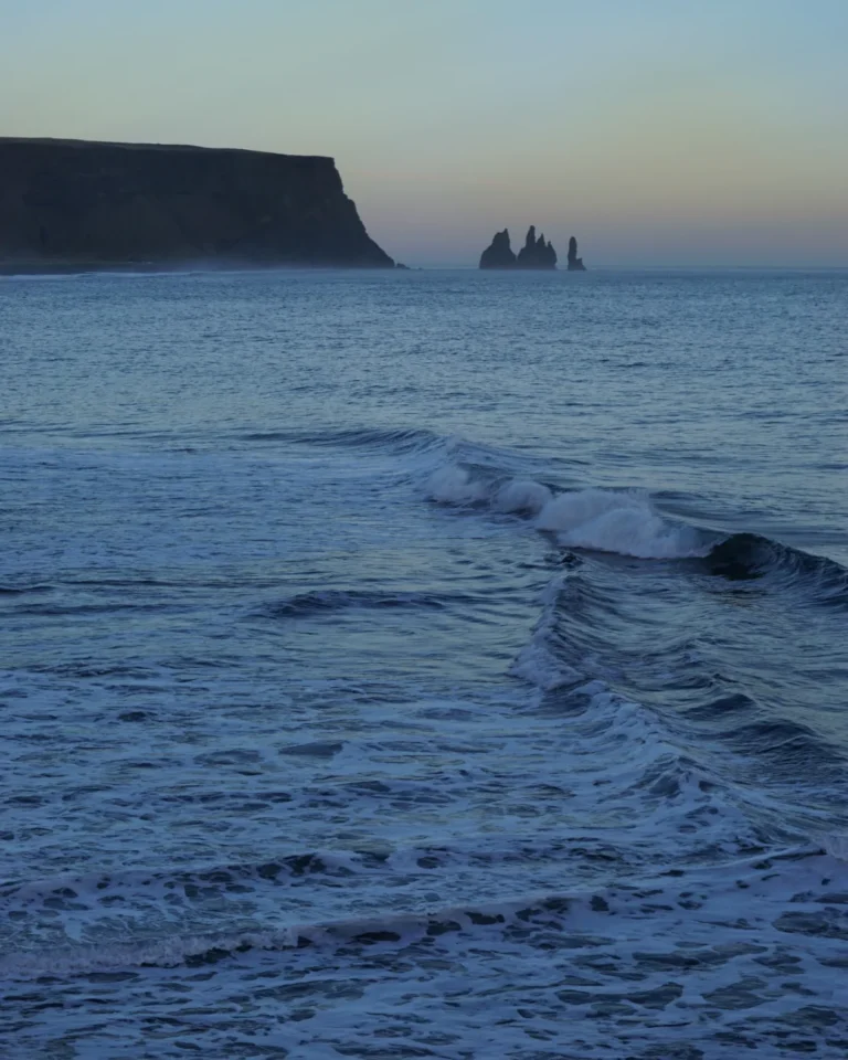 View of dramatic cliff formations rising from the sea, captured from Reynisfjara Black Sand Beach, Iceland