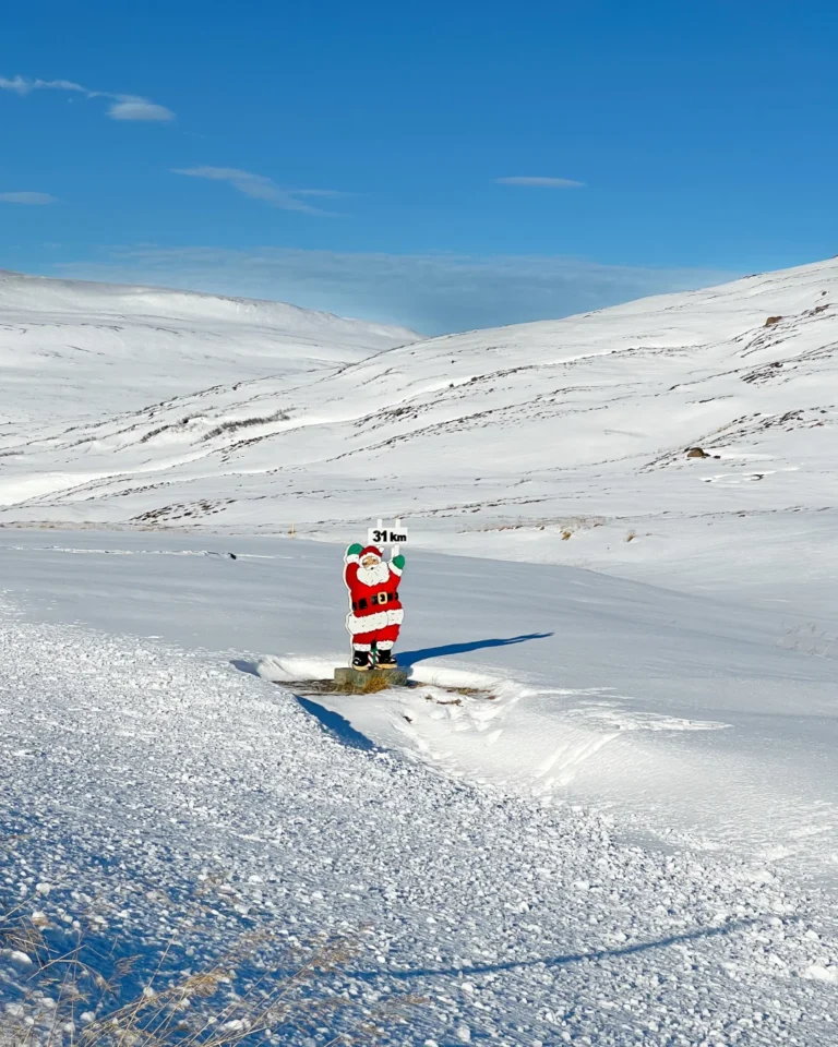 A wooden Santa figure covered in snow, with Icelandic mountains in the background