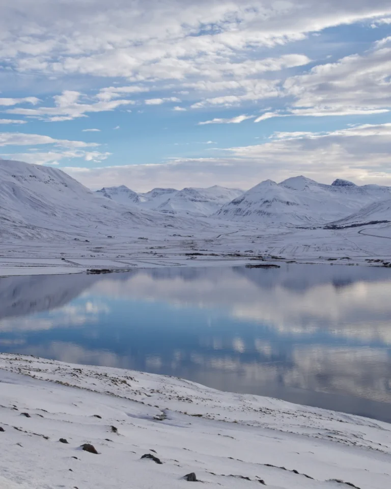 A snowy lake in Iceland reflecting the sky and surrounding snowy mountains