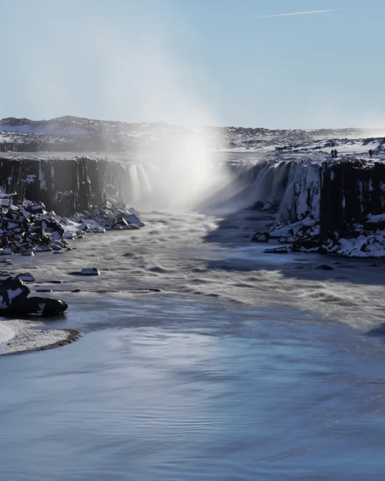 Telephoto shot of Selfoss waterfall surrounded by snow, under a clear blue sky