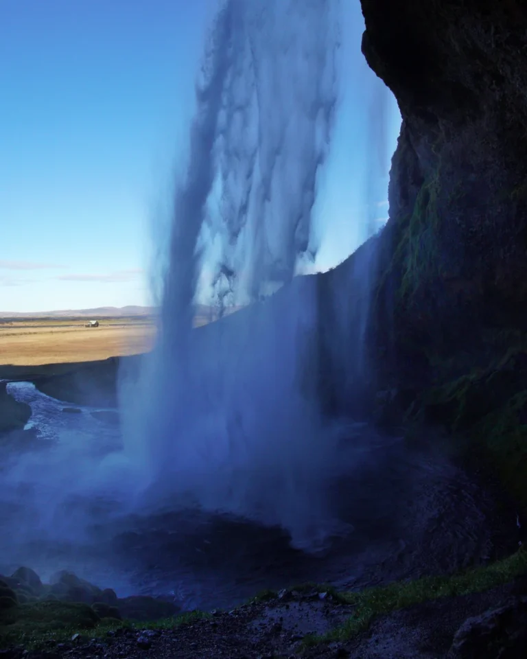 A view from behind Seljalandsfoss, showcasing cascading water and the vibrant Icelandic landscape beyond