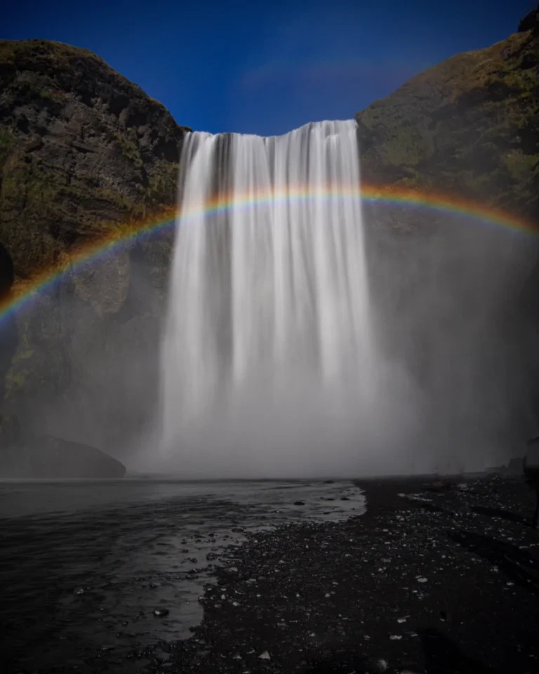 Skógafoss waterfall plunging into a misty pool with a vivid rainbow in the foreground, Iceland