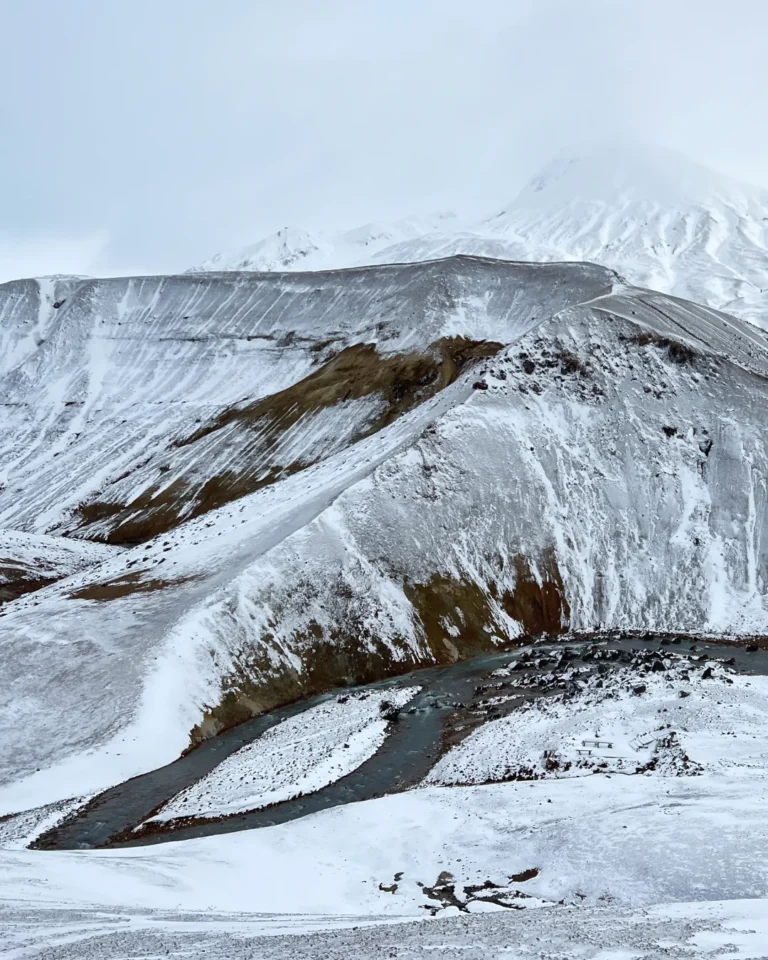 A steaming river meandering through bright white snowy mountains and rugged peaks in Hveradalir, Kerlingarfjöll, Iceland