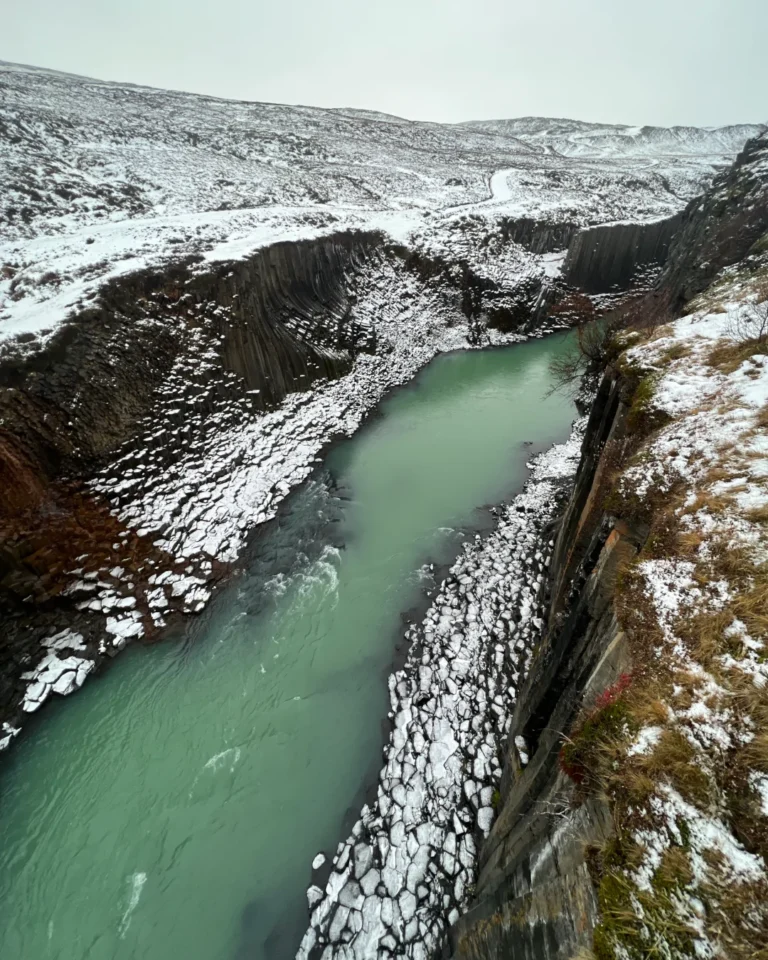 Aerial view of Stuðlagil Canyon covered in snow, showcasing its dramatic basalt columns, Iceland