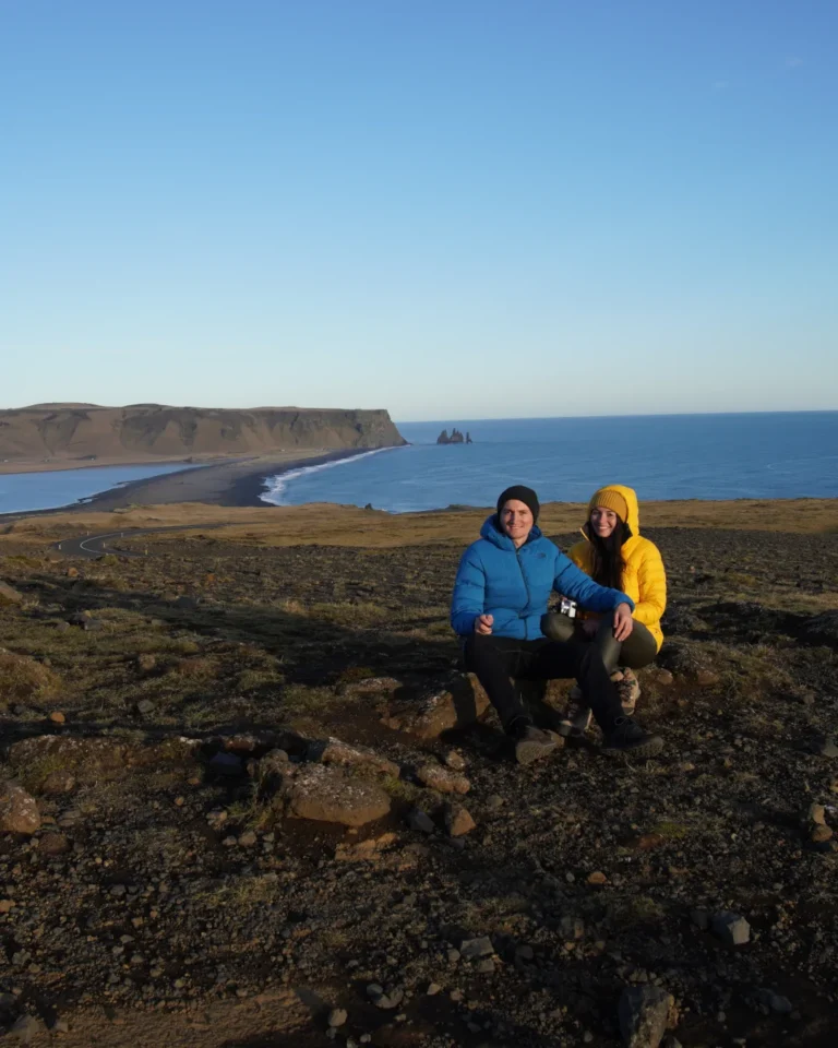 Us sitting on top of Dyrhólaey, overlooking the black sand beach in the sun in Iceland