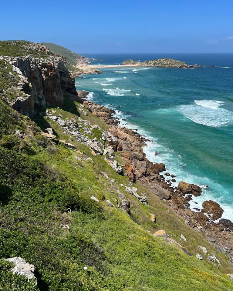 View from the upper hiking trail at Robberg Nature Reserve of cliffs and blue ocean waves.