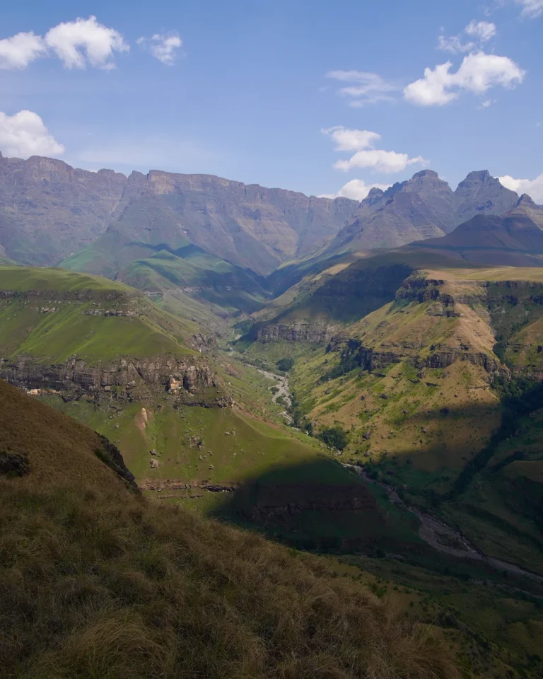 View from the Drakensberg summit into a green valley with a winding, dry riverbed.