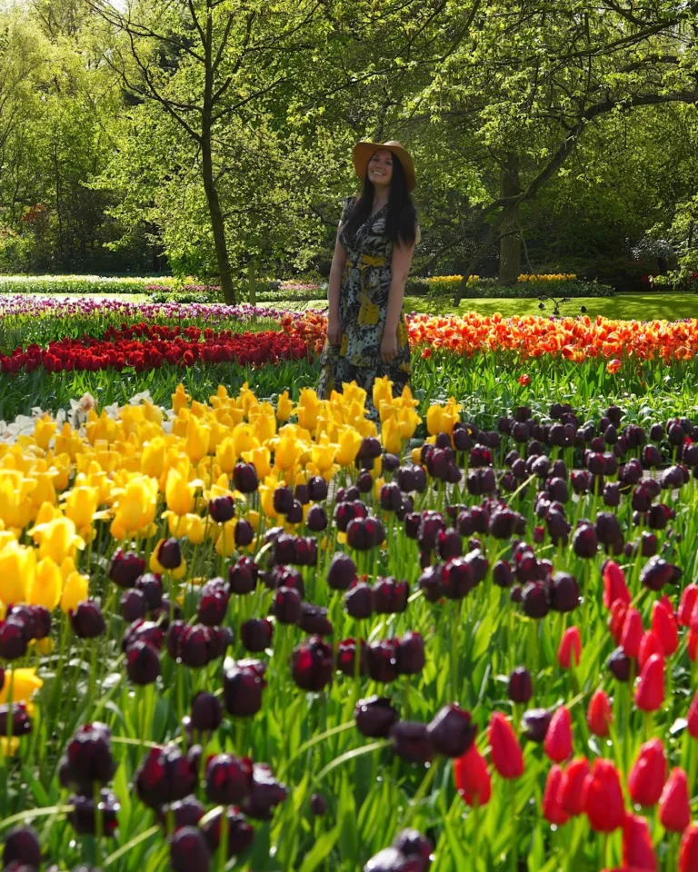 Junge Frau im gelben Kleid und Sonnenhut lacht inmitten bunter Tulpenbeete im Keukenhof Lisse.