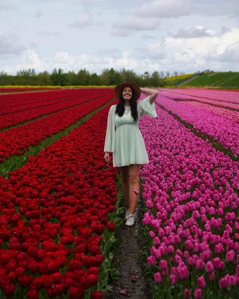 Frau im pastell-gruenen Kleid steht in einem Feld mit pinken und roten Tulpen in Flevoland, Niederlande.