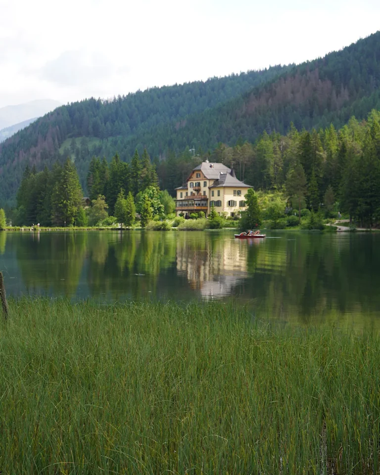 Ein gelbes, historisches Gebäude am Ufer des Toblacher Sees, das sich perfekt im glatten Wasser spiegelt.
