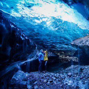 A couple inside Vatnajökull glacier, on there Iceland Adventure, surrounded by blue ice walls.