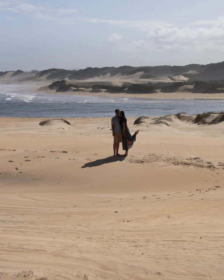 Travel couple standing in the sand dunes of Kenton-on-Sea with the ocean in the background.