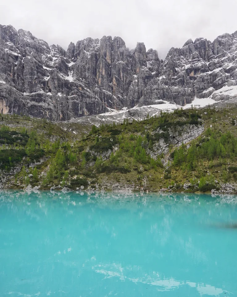 Wide-angle shot of Lake Sorapis surrounded by steep limestone cliffs of the Dolomites.