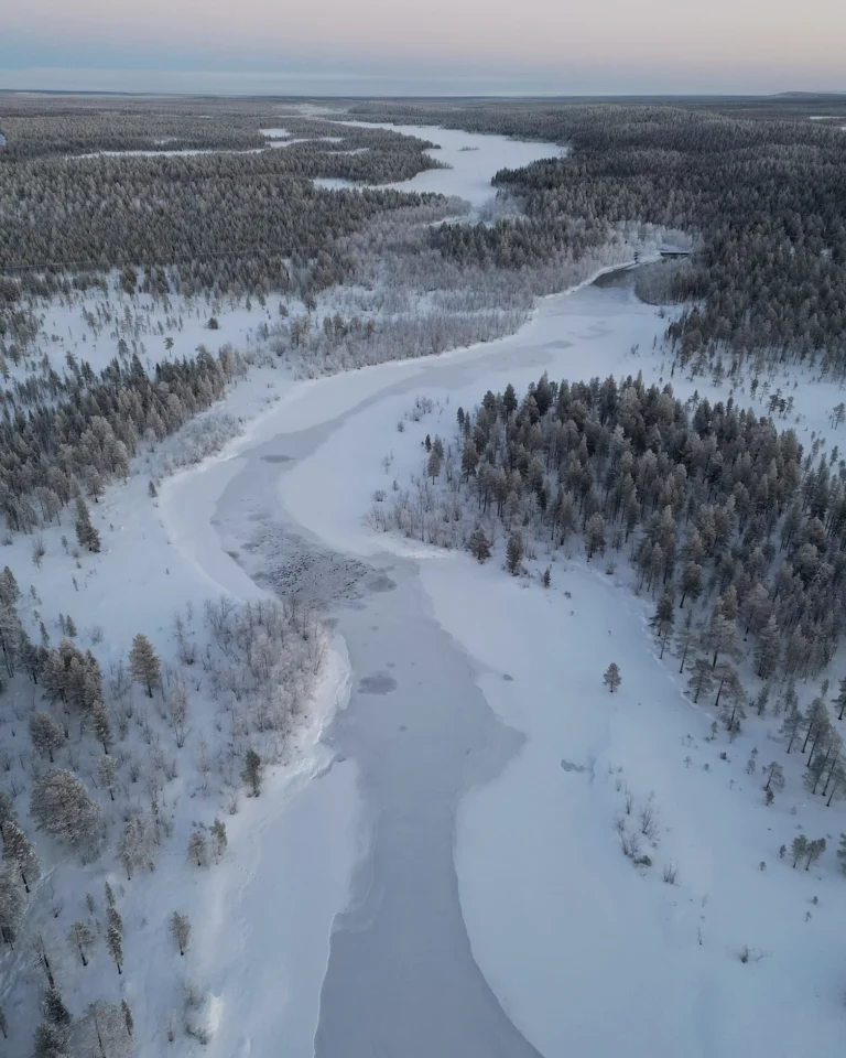 Aerial view of a wide, fully snow-covered river in the winter landscape of Lapland.