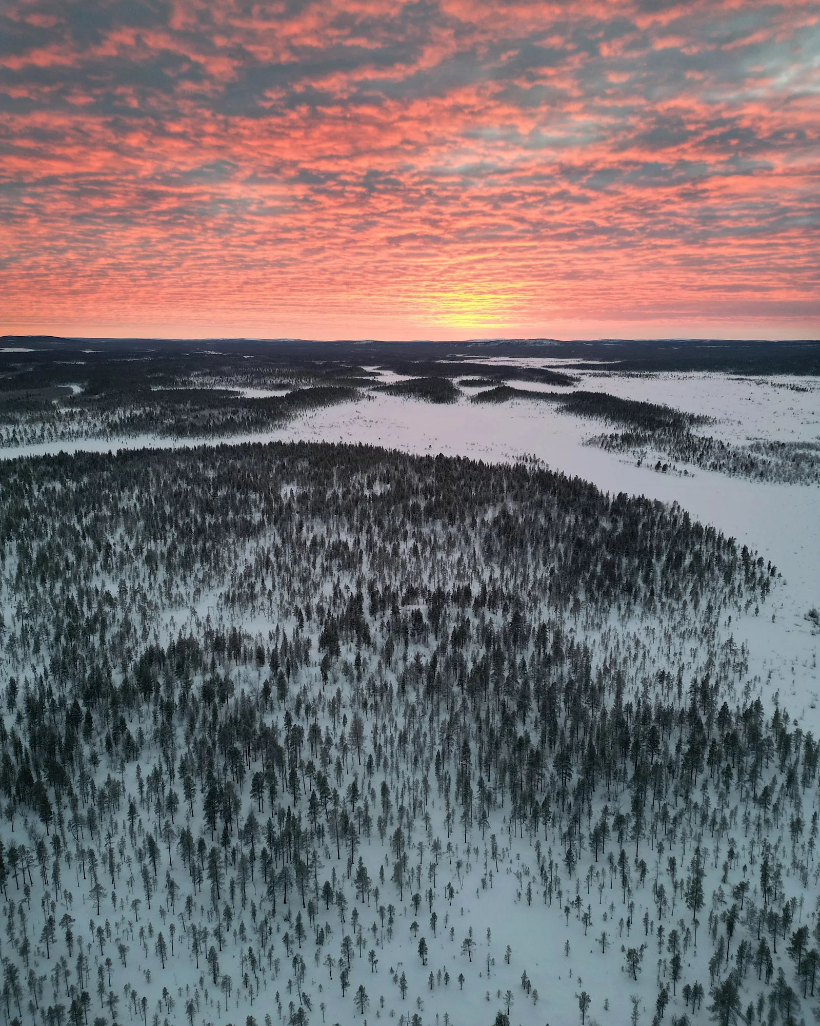 Drohnenaufnahme von verschneiter Landschaft in Lappland bei Sonnenuntergang.