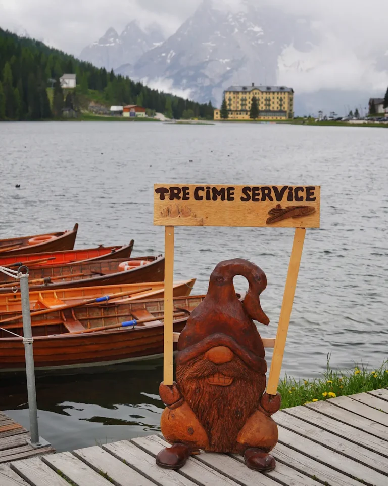 Blick über den Misurinasee auf das historische Grand Hotel vor den wolkenverhangenen Gipfeln der Dolomiten.
