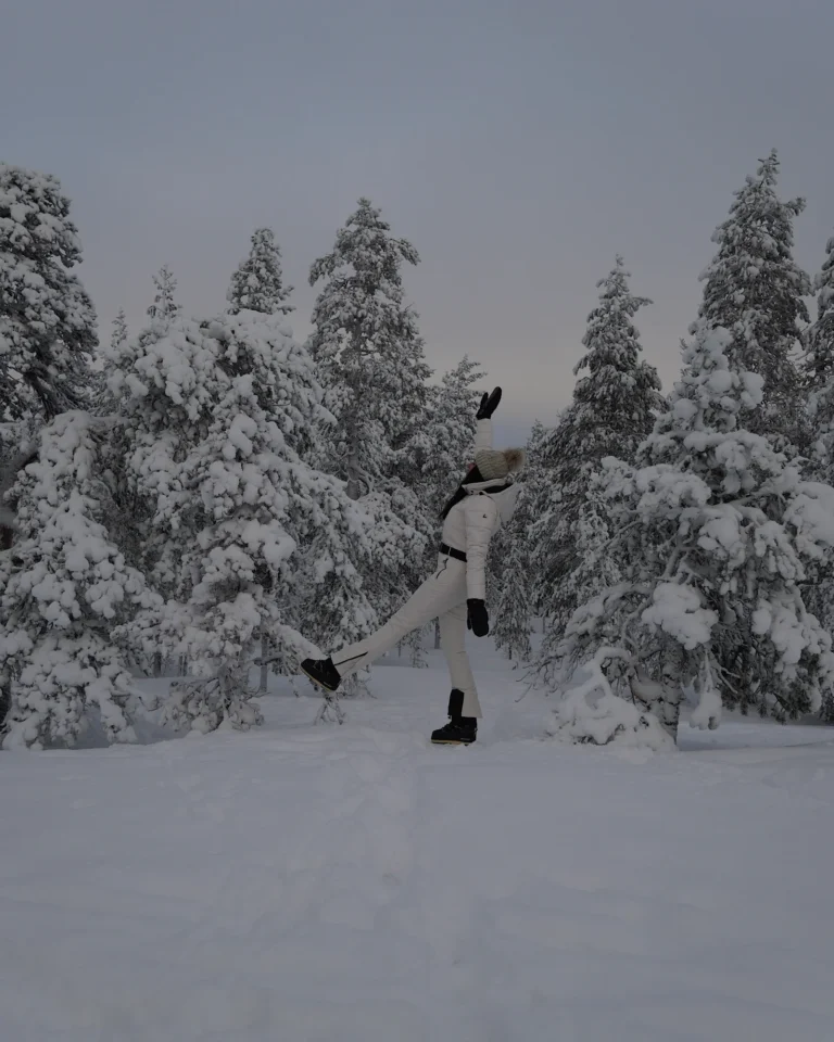 A woman standing in deep snow among snow-covered pine trees on Mount Ounasvaara in Rovaniemi.