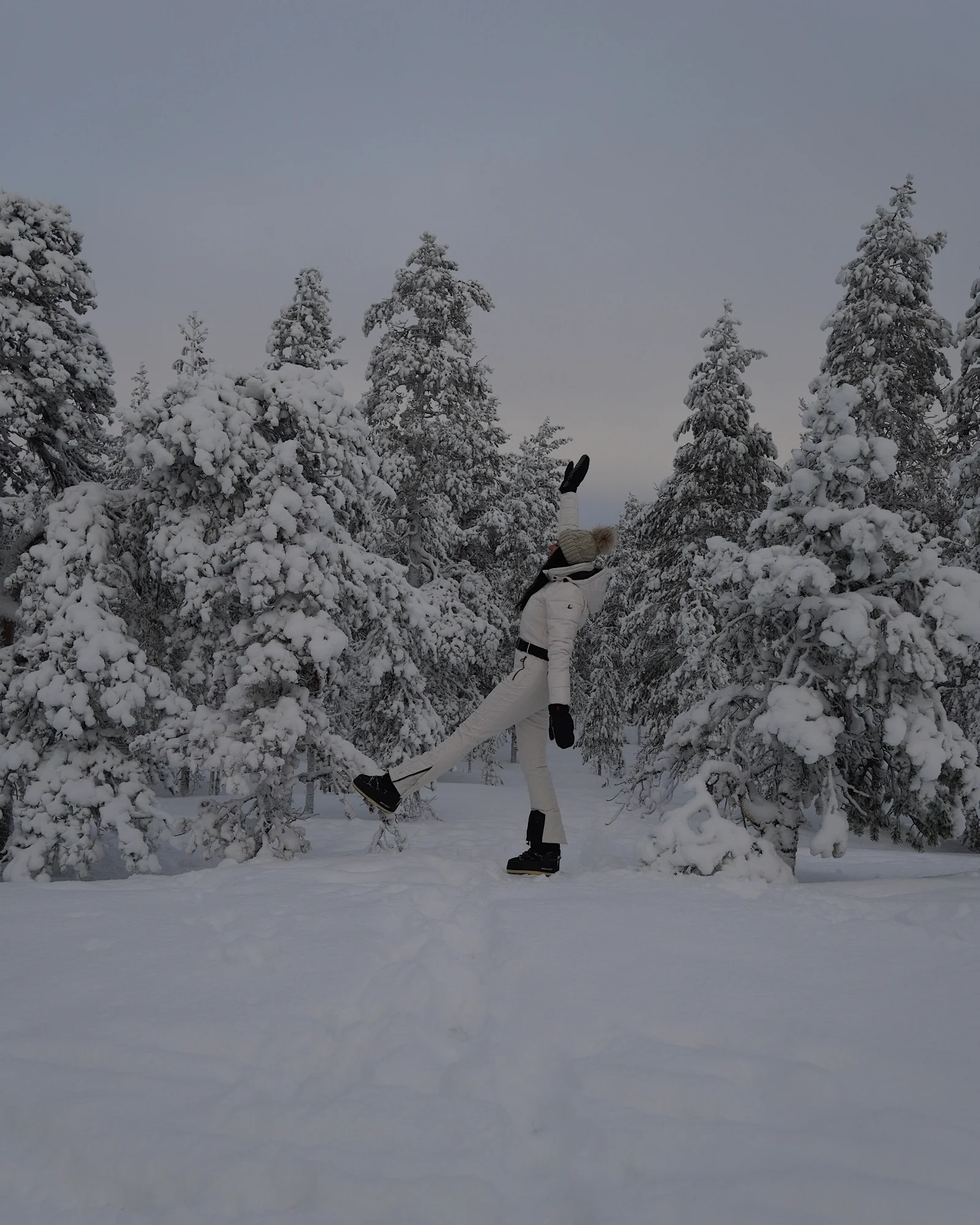 Eine Frau steht im tiefen Schnee zwischen verschneiten Tannen auf dem Berg Ounasvaara in Rovaniemi.
