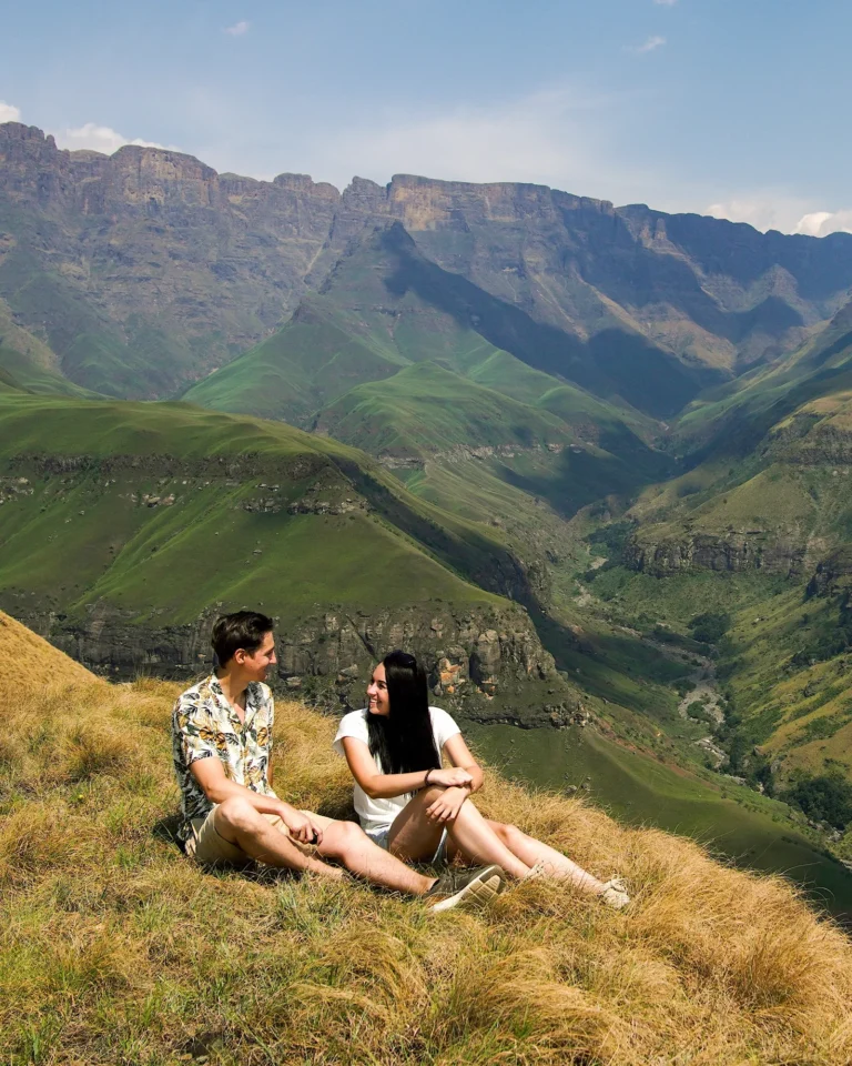 A young couple sitting on a meadow at the summit of the Drakensberg, looking at each other.