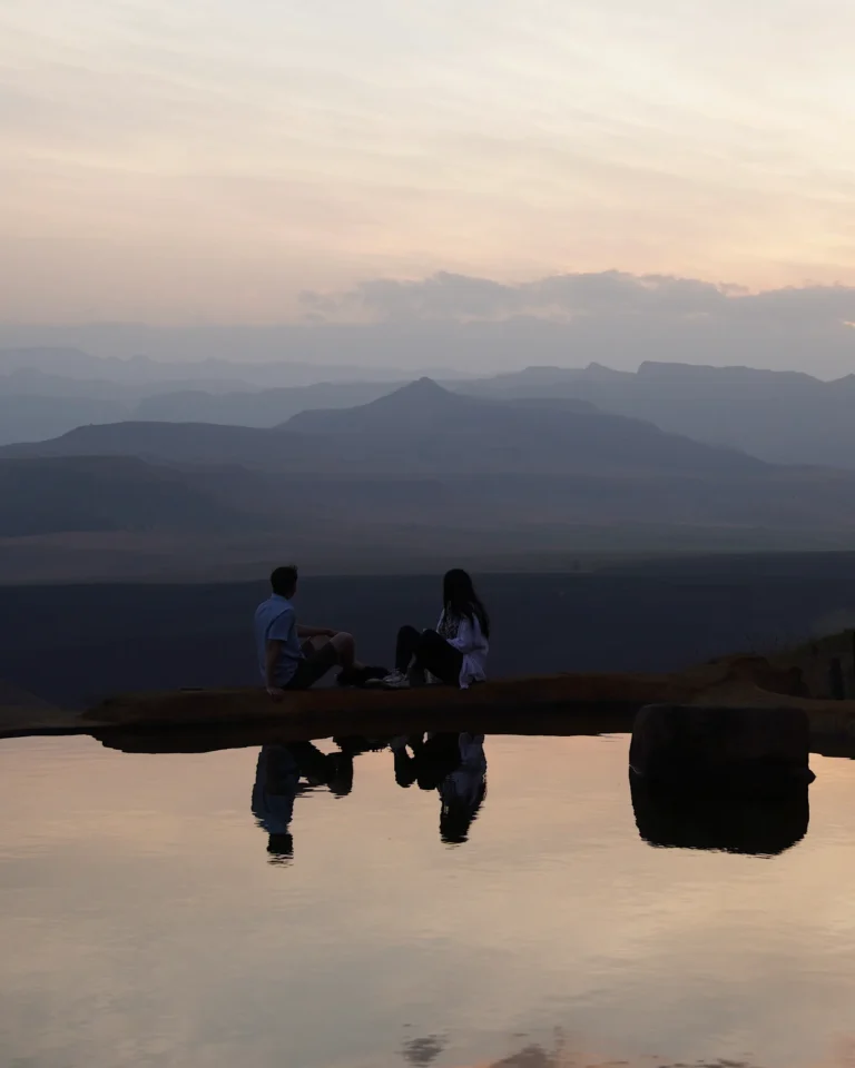 A couple sitting cross-legged by the pool at Berghouse and Cottages at sunset in Royal Natal National Park.