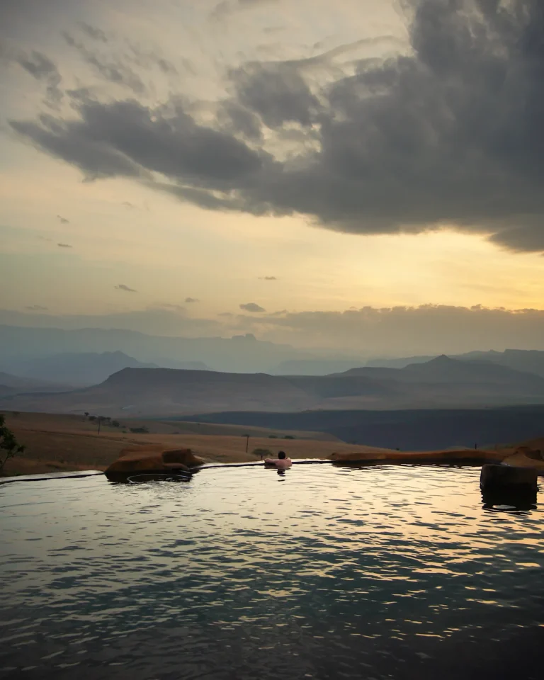 A man swimming in a naturally designed pool at Berghouse and Cottages at sunset in Royal Natal National Park.