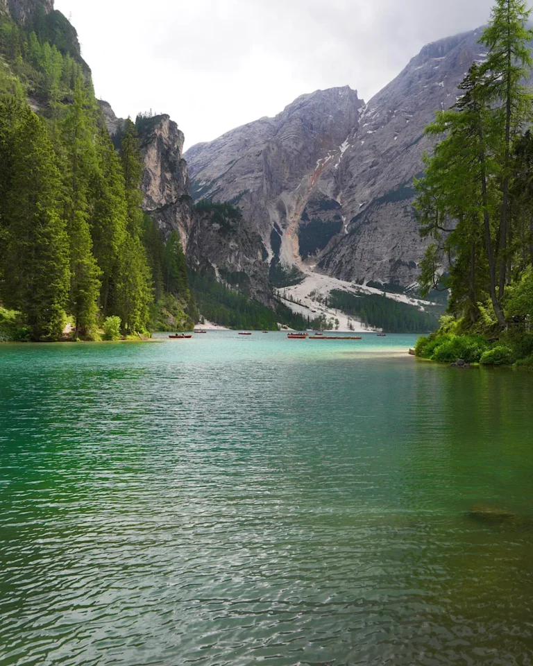 Türkisblauer Pragser Wildsee mit Holzbooten und dem Bergmassiv des Seekofel bei Sonnenschein.